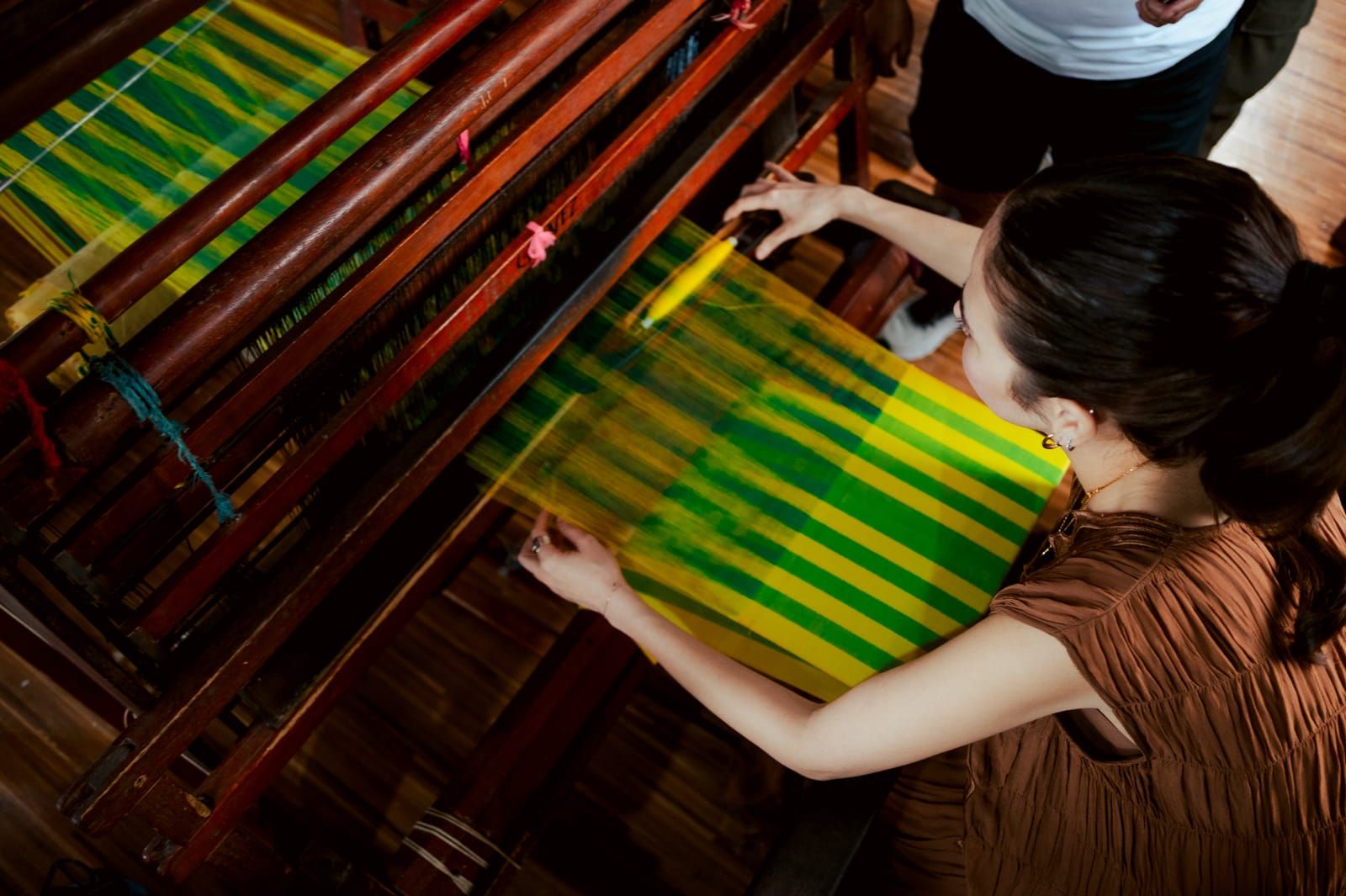 Bela Padilla guiding green and yellow threads on the loom