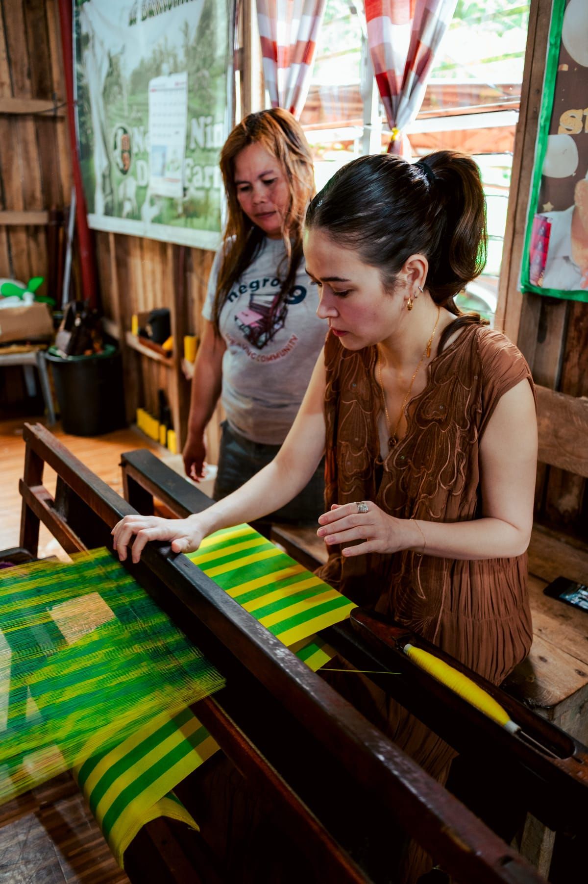 Bela Padilla weaving green and yellow fabric beside a weaver