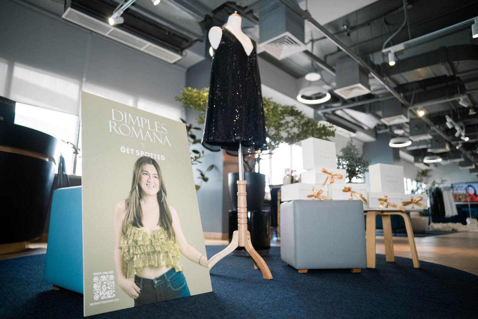 The Dimples Romana x Get Spotted poster beside a black sequin dress from the collection at the launch