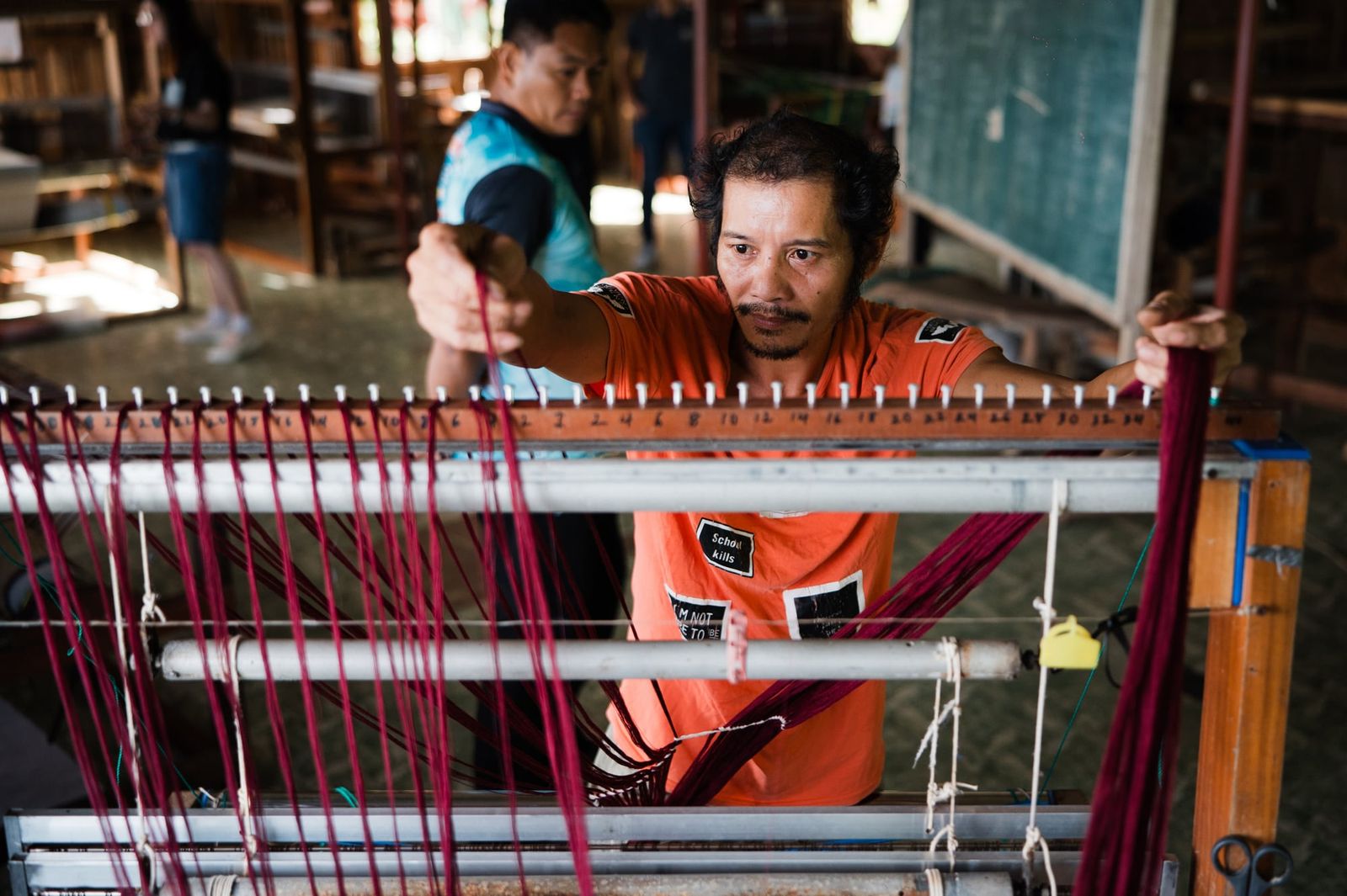 A weaver threading a loom with deep red yarn