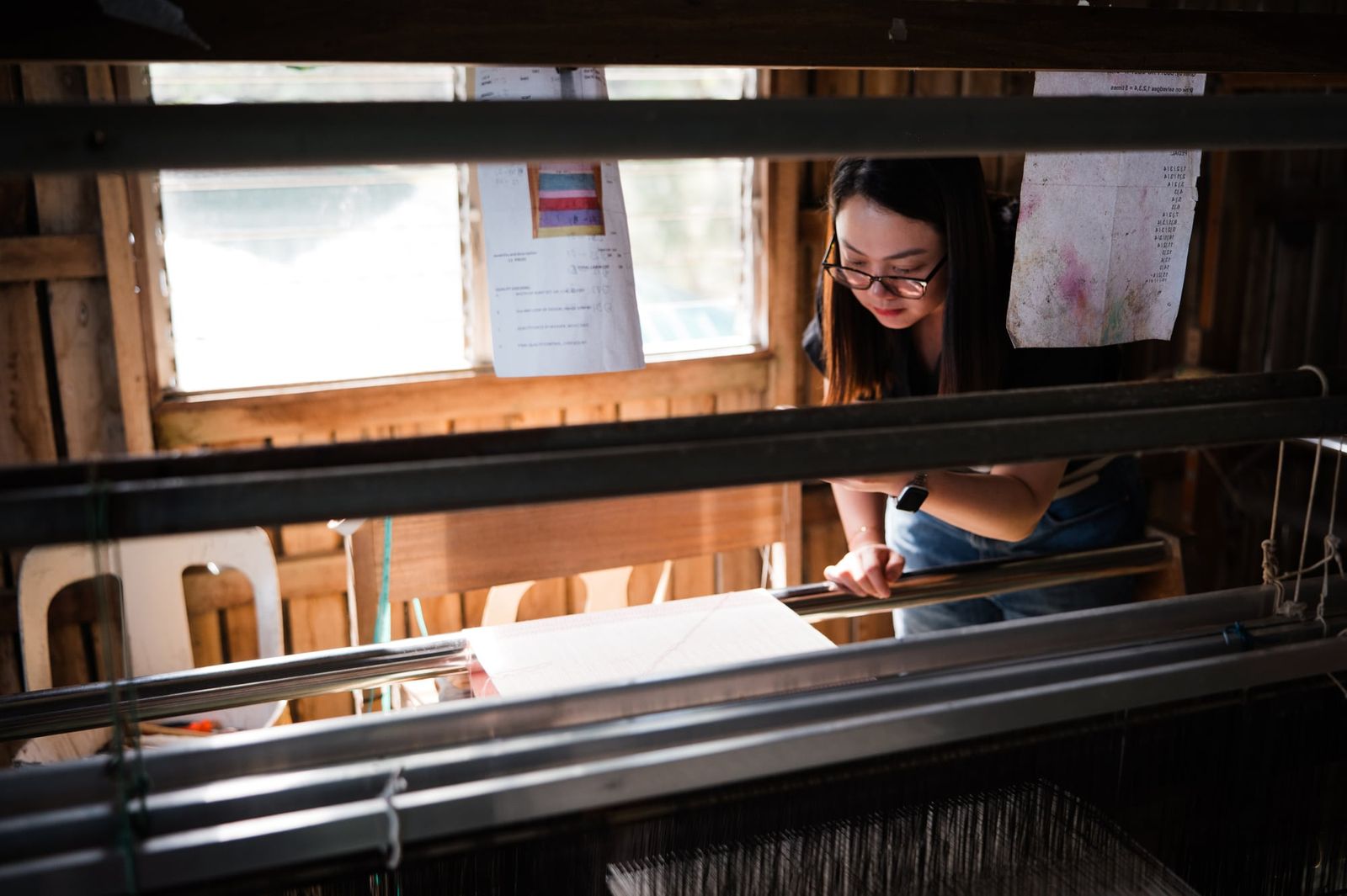 A weaver at a wide loom by the window