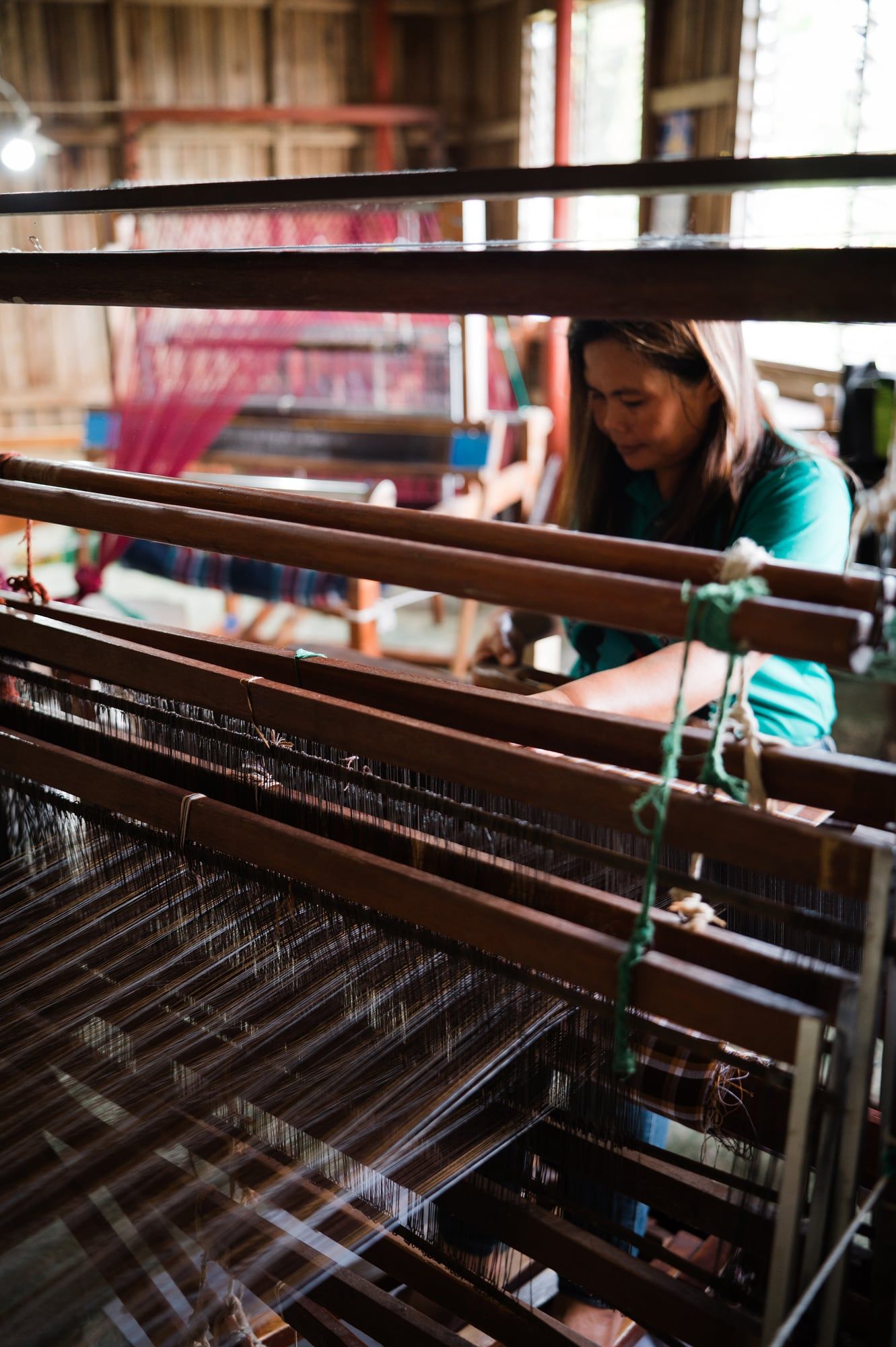 A weaver focused on her loom, threads stretched in front of her