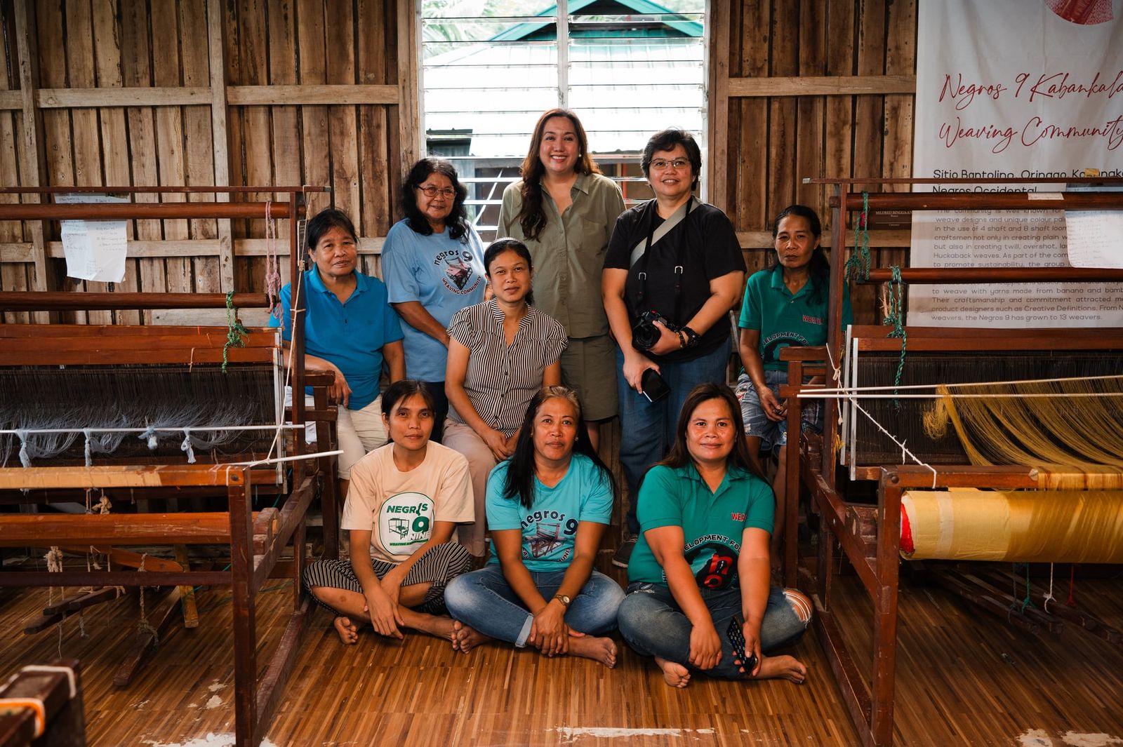 The Negros Nine Weavers with the Get Spotted team in front of the looms and the Negros 9 Kabankalan Weaving Community banner